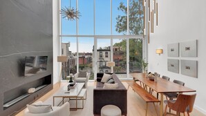 A modern living room with a large window, a fireplace, and a dining area with a wooden table and chairs.