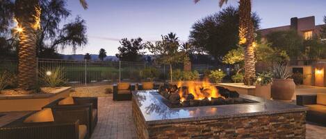 An outdoor patio with a stone fire feature, wicker furniture, and palm trees.