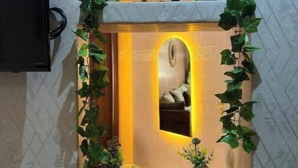 Een klein, verlicht nisje met een spiegel en planten in potten, omlijst door een decoratieve boog.