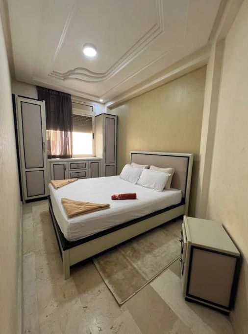 A bedroom with a bed, a nightstand, a wardrobe, and a window with curtains.