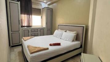 A bedroom with a bed, a nightstand, a wardrobe, and a window with curtains.