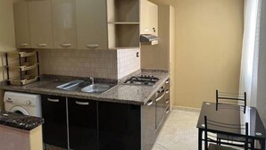 Een kleine keuken met een dubbele spoelbak, een fornuis en een eethoek met een tafel en stoelen.