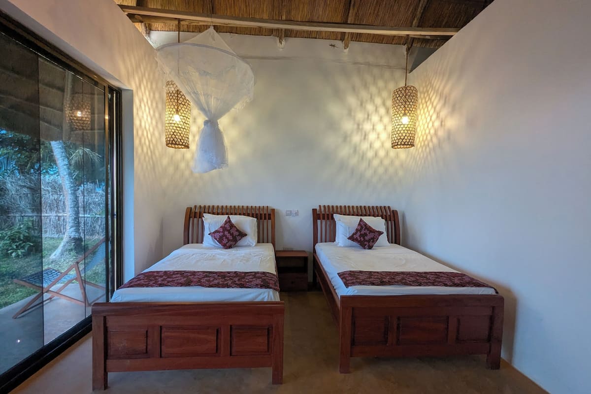 Quarto com duas camas de madeira, uma janela grande e duas luzes fixadas na parede.