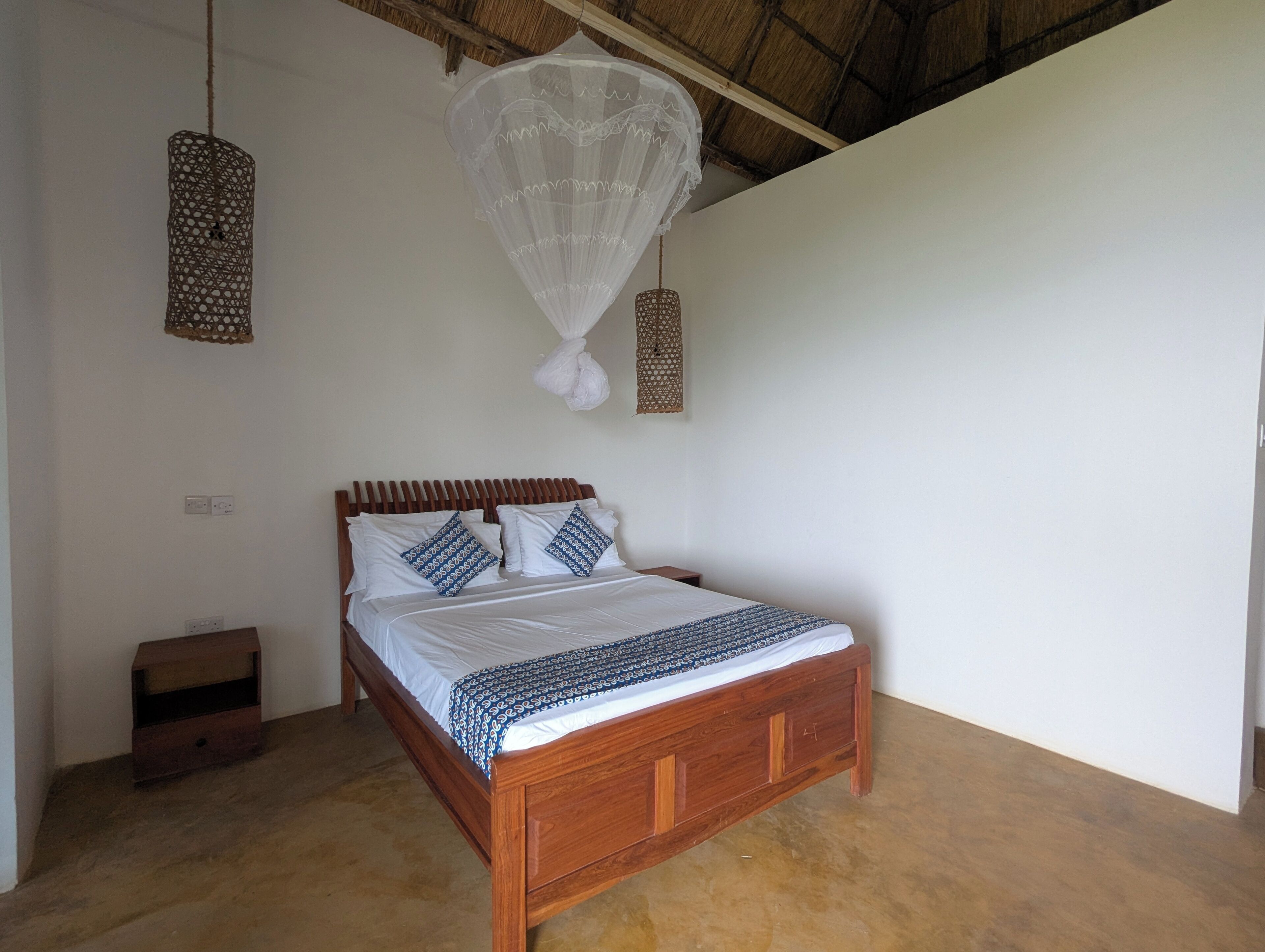 A bedroom with a wooden bed, white bedding, and hanging mosquito nets.