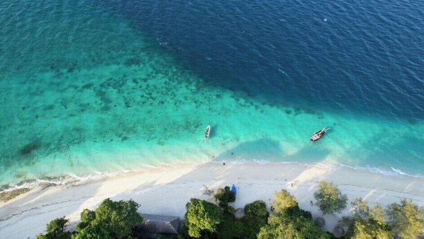 Vista aérea de uma praia com águas turquesa cristalinas, areal arenoso e barcos.