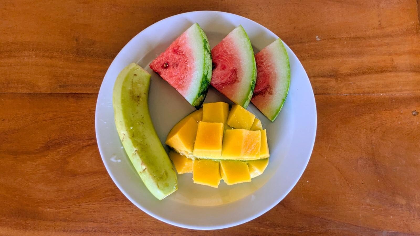 A plate with watermelon, mango, and avocado on a wooden table.