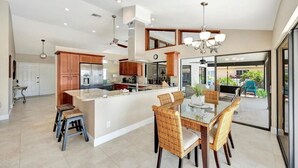 A modern kitchen with a central island, wooden cabinets, and a dining area with wicker chairs.
