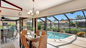 A modern indoor pool area with a glass enclosure, wicker furniture, and a view of the surrounding landscape.
