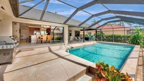 A modern outdoor pool area with a covered patio, a barbecue grill, and a dining area.