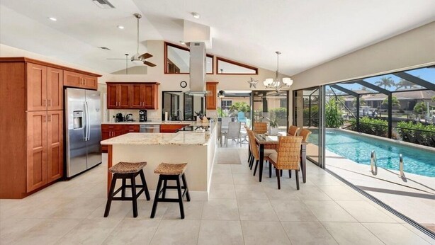 A modern kitchen with a large island, wooden cabinets, and a view of a swimming pool.