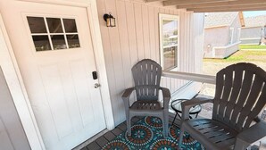 Un portico con due poltrone Adirondack, una porta bianca e un tappeto decorato.