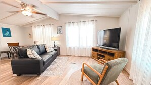 Un soggiorno con un divano nero, un tavolino in legno e un televisore su un mobile in legno.