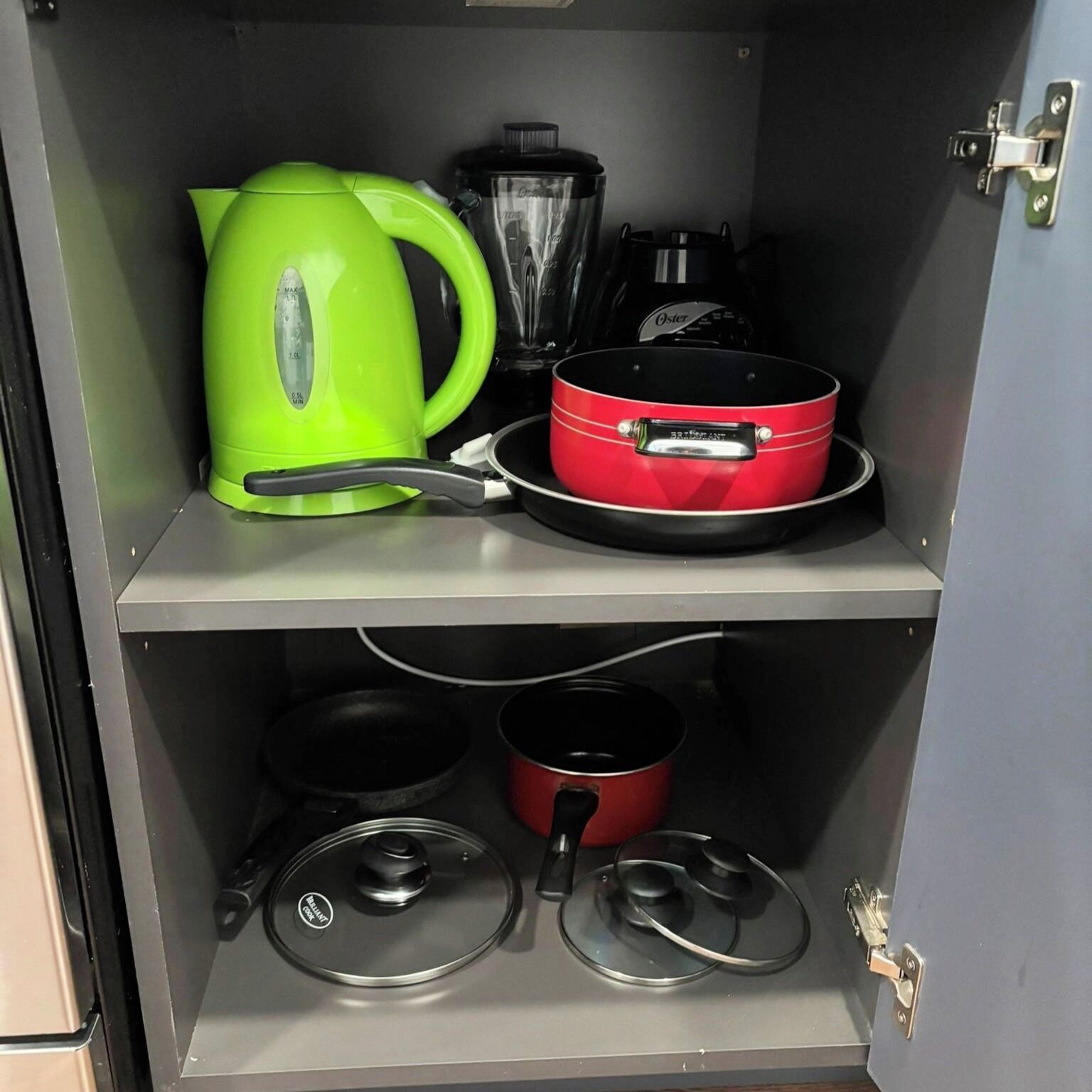 A kitchen with a kettle, a red pot, and two lids on the counter.