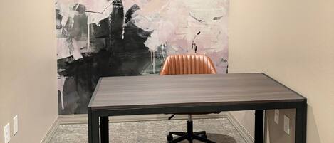 Une salle de conférence avec une grande table en bois foncé, une seule chaise orange et un grand tableau abstrait accroché au mur.