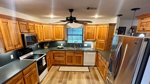 A modern kitchen with wooden cabinets, stainless steel appliances, and a black ceiling fan. - Waterfront Getaway - With Boat Parking and Access to Lake Conroe!! (Willis)