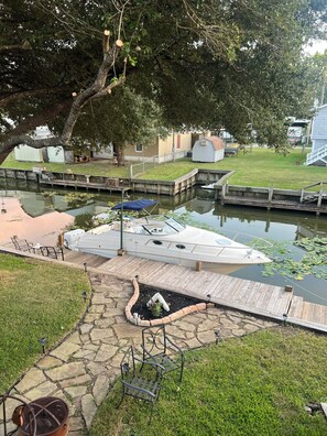 A boat docked at a marina with a wooden dock, stone pathway, and a grassy area with a small shed in the background. - Waterfront Getaway - With Boat Parking and Access to Lake Conroe!! (Willis)