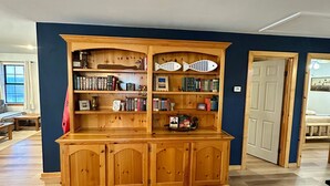 A room with a wooden cabinet containing books and decorative items. - Waterfront Getaway - With Boat Parking and Access to Lake Conroe!! (Willis)