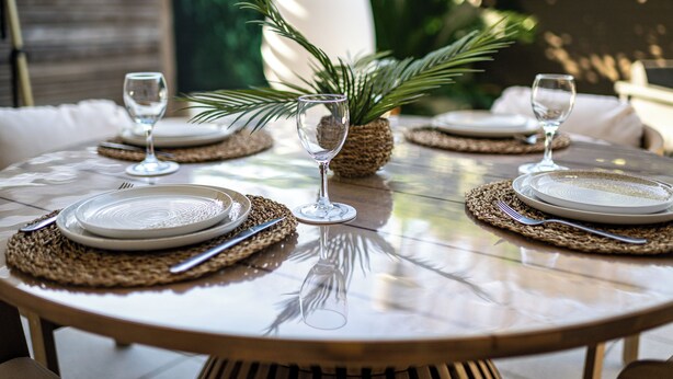 Een ronde eettafel met placemats, borden en wijnglazen, gedekt voor een maaltijd.