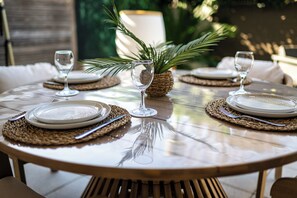 Une table de salle à manger ronde, avec des sets de table, des assiettes et des verres à vin, prête pour le repas.