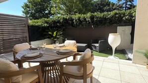 Een terras buiten met een ronde tafel voor vier personen, omringd door houten stoelen met kussens.