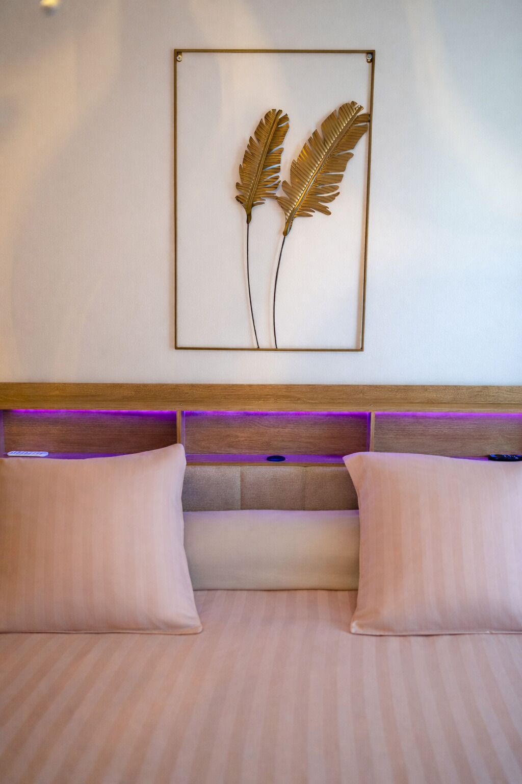 A bedroom with a bed, two pillows, a headboard with a wooden panel, and a wall-mounted artwork of two leaves.