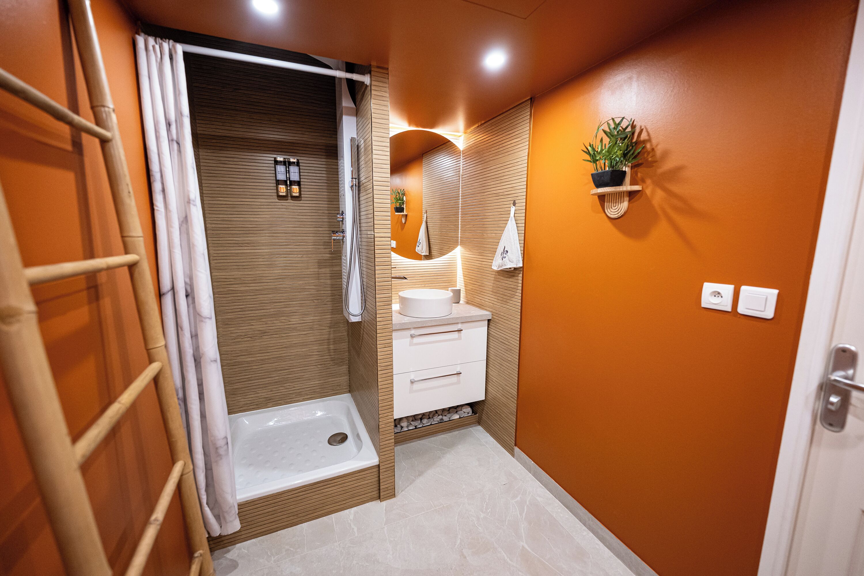 A modern bathroom with a shower, toilet, and sink, wooden paneling, and a potted plant on the wall.