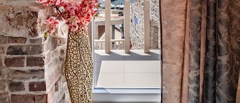 A room with a stone wall, a large vase with pink flowers, and a view of a marina and buildings.