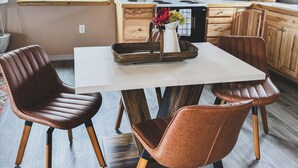 A modern kitchen with wooden cabinets, a dining table with chairs, and a window with a view of a fence. - Scenic Studio Retreat- Steps to Goldbug Hot Springs (Salmon)