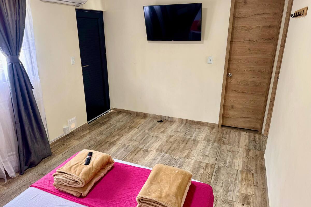 A hotel room with a bed, a TV mounted on the wall, and a wooden door.