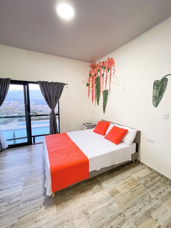 A bedroom with a bed, a nightstand, a window with curtains, and a wall with a floral mural.
