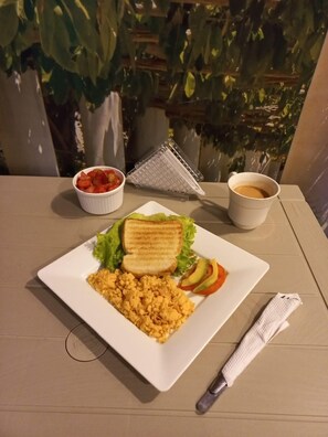 A breakfast plate with scrambled eggs, toast, lettuce, tomato, and avocado, a cup of coffee, and a grater on a table with a napkin. - Best View Aparta Hotel (Dosquebradas)