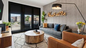 Un salon moderne avec un canapé gris, une table basse ronde en bois et un panneau décoratif portant l'inscription « Nashville » au mur.