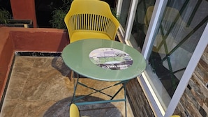 Un petit espace extérieur aménagé avec une table ronde et deux chaises jaunes.