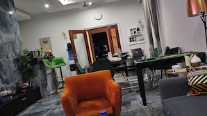 Un salon moderne avec un sol en marbre, un lustre, un fauteuil orange, un canapé et un coin repas à l’arrière-plan.