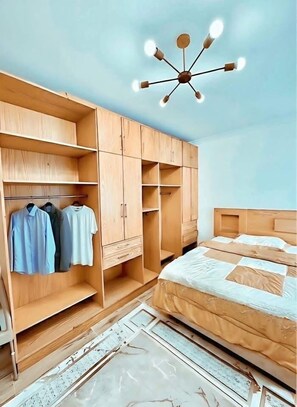 Une chambre avec une armoire en bois, un lit avec une literie blanche et un luminaire fixé au plafond.
