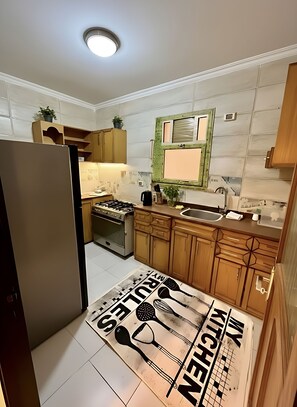 A kitchen with wooden cabinets, a gas stove, a sink, and a backsplash with a window. - Stylish Apt at Jannah Zayed Compund , Egypt (El Sheikh Zayed City)