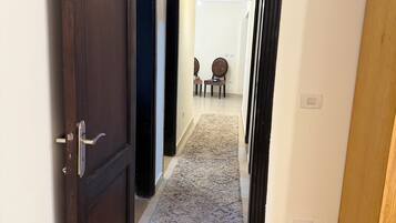A hallway with a wooden floor, a carpeted area, and a door leading to another room.