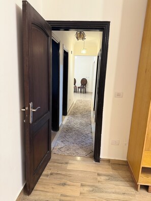 A hallway with a wooden floor, a carpeted area, and a door leading to another room. - Stylish Apt at Jannah Zayed Compund , Egypt (El Sheikh Zayed City)