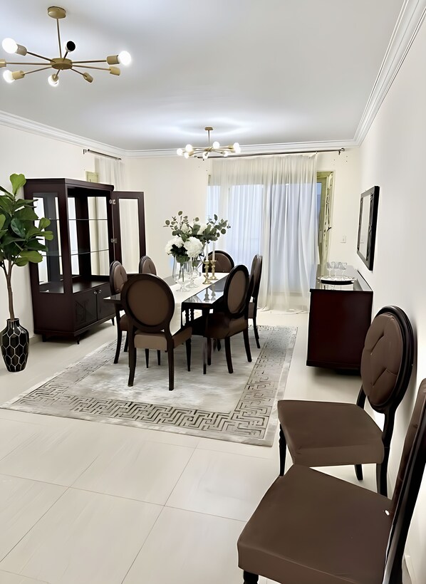 A modern dining area with a round table, chairs, a vase with flowers, and a decorative rug.