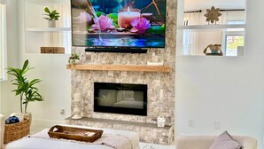 Una sala de estar con chimenea de piedra, un televisor de pantalla plana montado encima y una zona de estar cómoda con un sofá y una butaca.