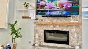 Una sala de estar moderna con un televisor de pantalla plana montado en una pared de piedra, una chimenea debajo y un estante con objetos decorativos.