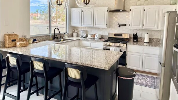 Una cocina moderna con armarios blancos, una isla grande con taburetes de bar, una estufa a gas e iluminación colgante.