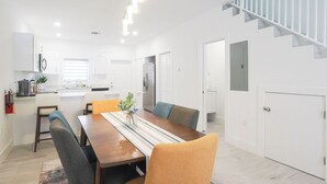 A modern kitchen with white cabinets, a dining area with a wooden table and chairs, and a staircase with a white railing. - New 2 bed townhome near Blowholes in East End (Grand Cayman)