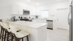 A modern kitchen with white cabinetry, a central island with bar stools, a built-in microwave, and a dishwasher. - New 2 bed townhome near Blowholes in East End (Grand Cayman)