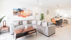 A modern living room with a sectional sofa, a coffee table, and a dining area with chairs and a table. - New 2 bed townhome near Blowholes in East End (Grand Cayman)