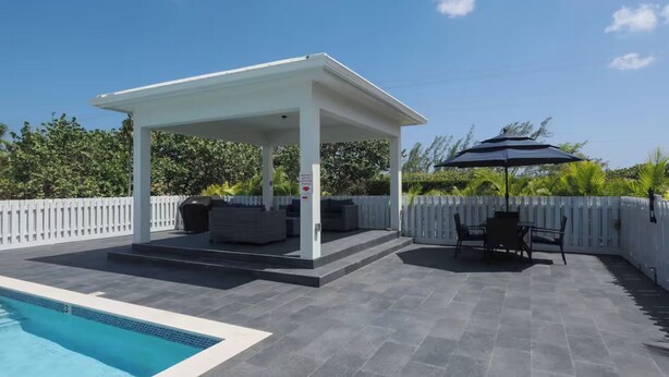 A covered outdoor area with a pool, seating, and a pergola. - New 2 bed townhome near Blowholes in East End (Grand Cayman)