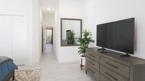 A modern living room with a large flat-screen TV, a wooden cabinet, a mirror, and a potted plant. - New 2 bed townhome near Blowholes in East End (Grand Cayman)