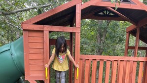 A wooden play structure with a slide and climbing steps.