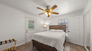 A bedroom with a wooden bed, a ceiling fan, a bench, and a door. - Lake Whitney 3BR getaway: family-ready, boat-friendly, Wi-Fi, fire pit (Laguna Park)
