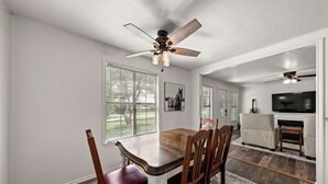 A dining area with a wooden table and chairs, a ceiling fan, and a television in the background. - Lake Whitney 3BR getaway: family-ready, boat-friendly, Wi-Fi, fire pit (Laguna Park)